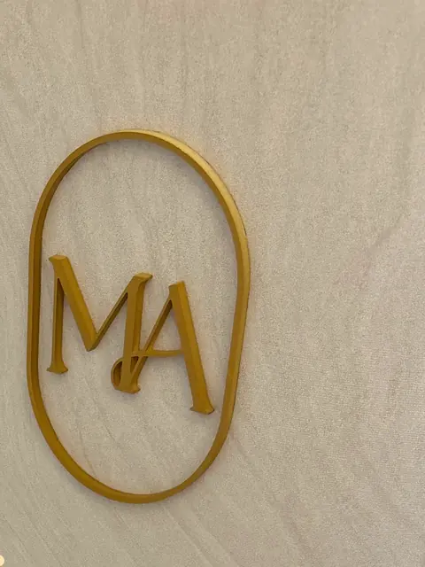 O monograma MA dourado na parede do consultório